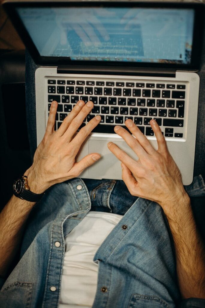 A man in casual attire works remotely, typing on a laptop. Captured from above.