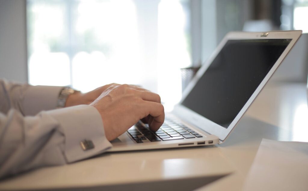 Close-up of hands typing on a laptop in a bright, modern office setting.