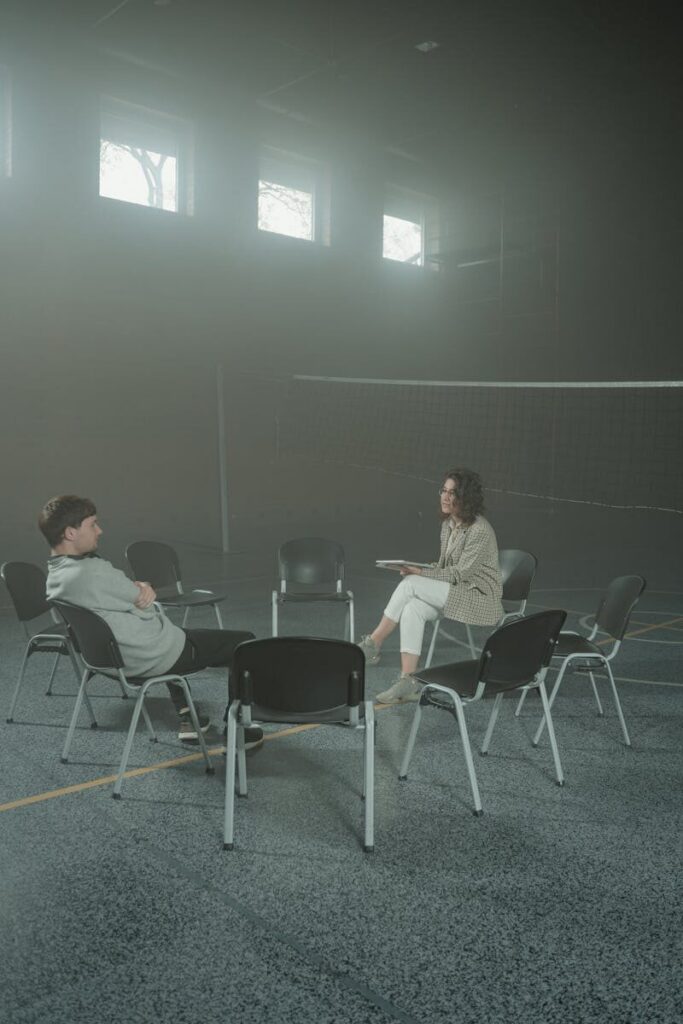 A man and woman engaged in a one-on-one therapy session in an empty gymnasium.