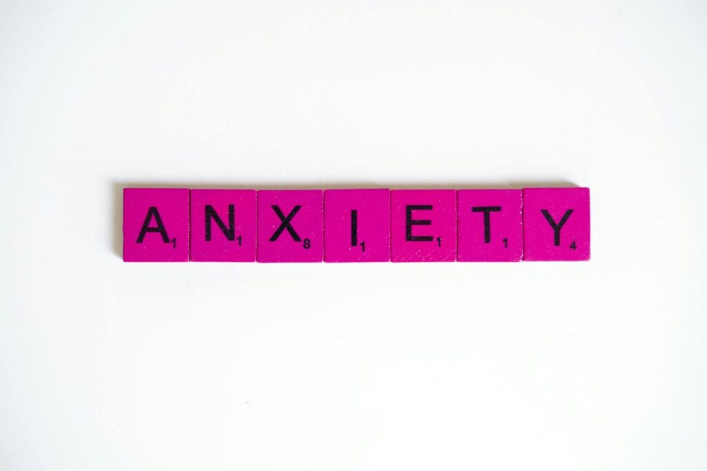 Pink Scrabble tiles spelling 'anxiety' on a white surface. Concept of mental health.