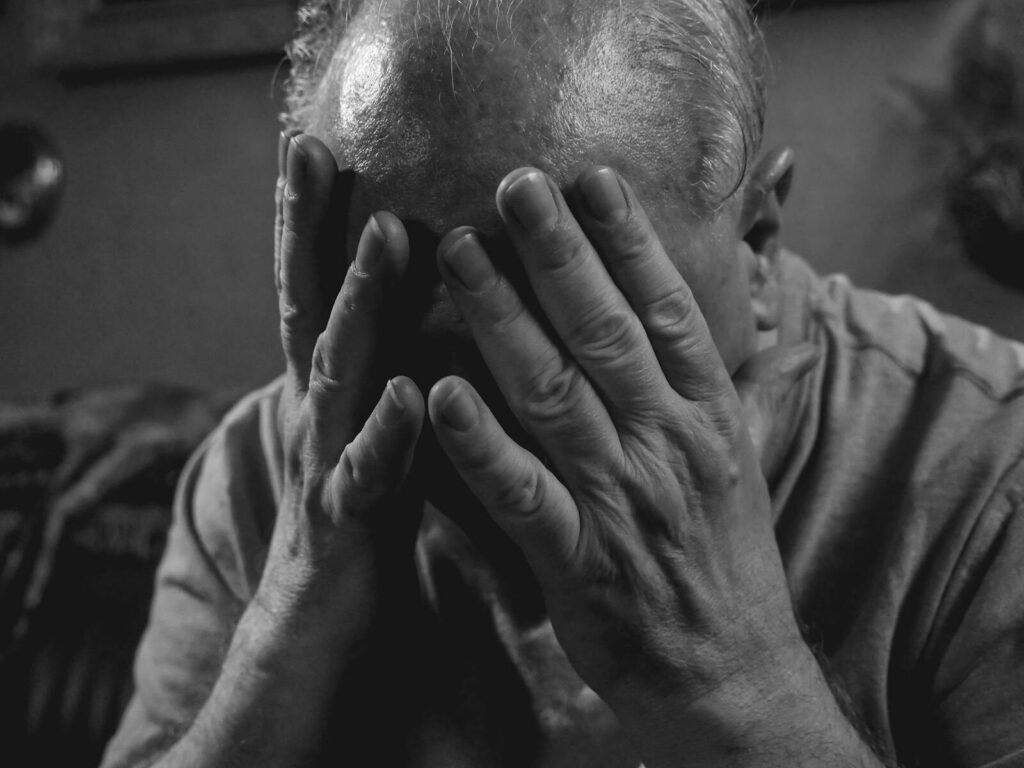 Elderly man covering face with hands, evoking emotions of sadness and stress.