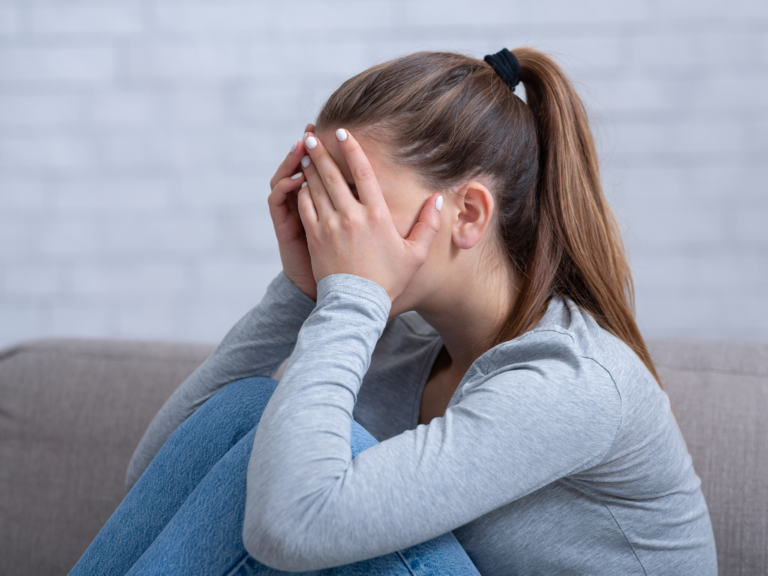 Kobieta siedzi na podłodze z głową ukrytą w dłoniach, symbolizując emocjonalne skutki traumy po napaści seksualnej.